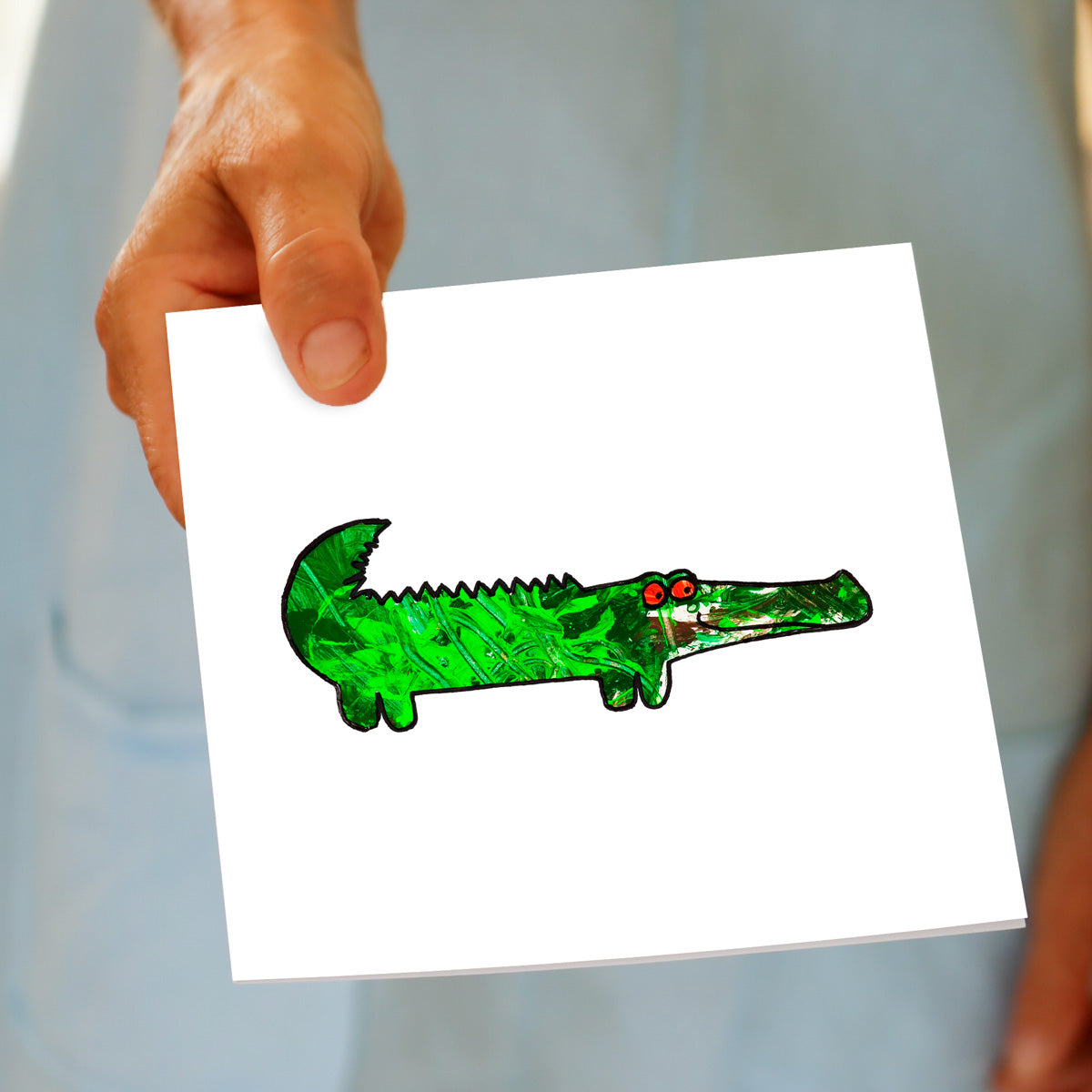 Colourful kids drawing of a allligator on a white background greeting card, being held by hand. A quality greeting card found at Golly Gosh Creations.