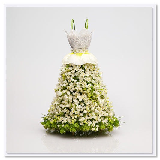 Floral dress made of white blossoms with intricate lace bodice, full skirt, green calla lily straps, and green flowers at base against white background.