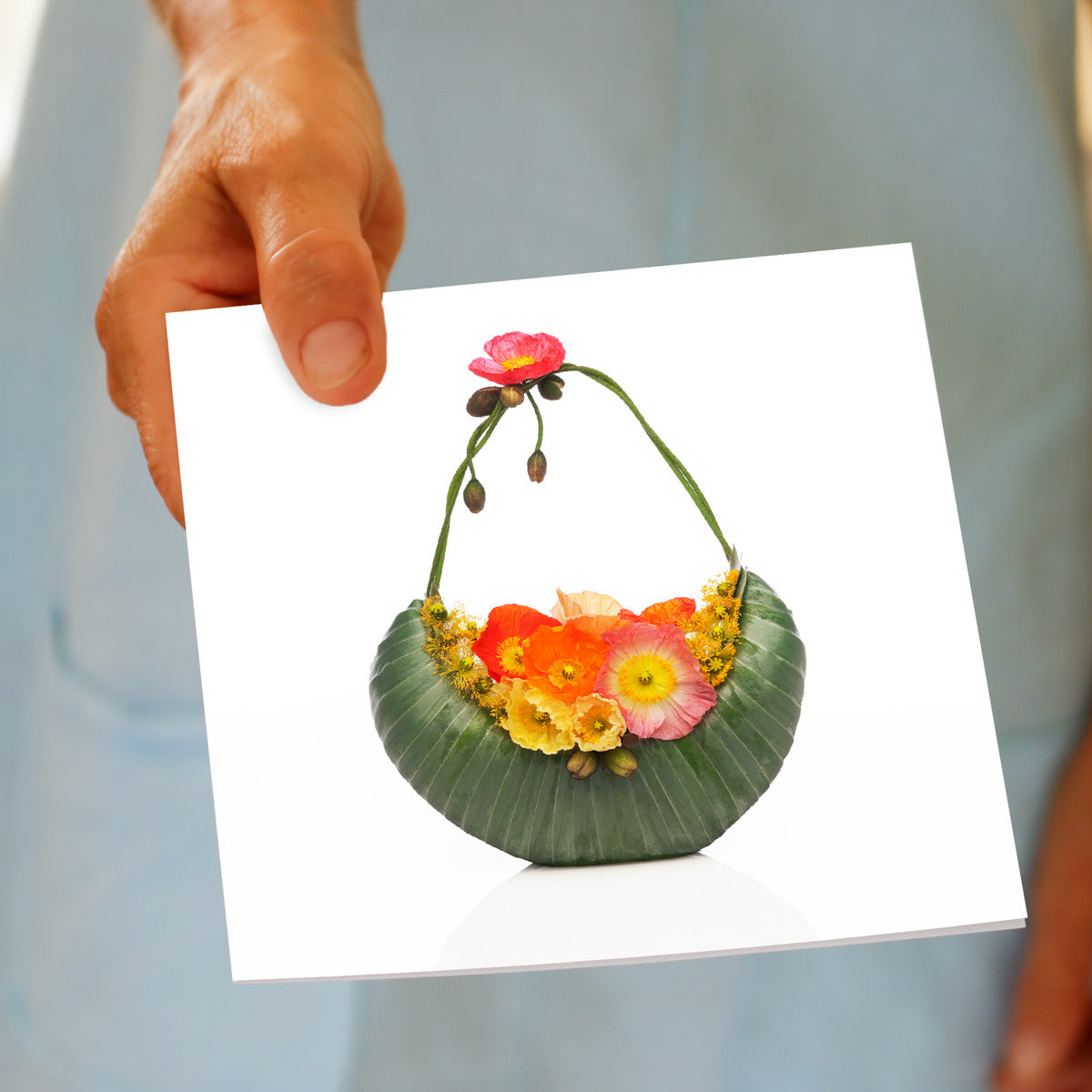 A hand held poppy bag greeting card from Golly Gosh Creations. A generous square card crafted from vibrant wild poppies and soft leucadendron leaves.