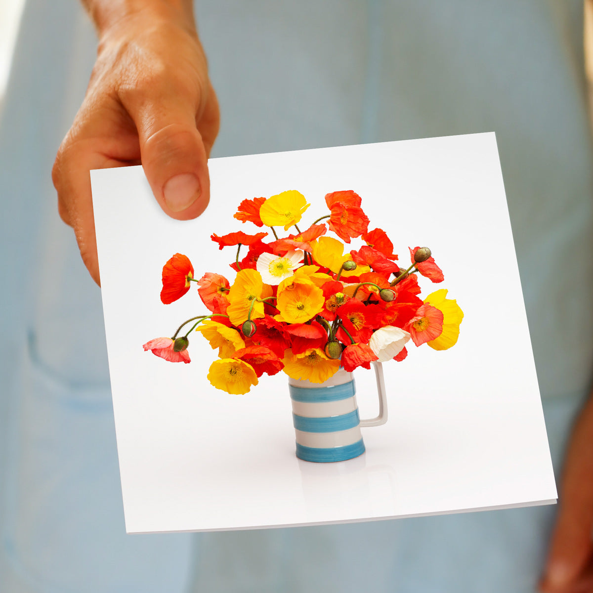 A hand held poppy jug greeting card from Golly Gosh Creations. Displaying delightful vibrant wild poppies in a classic blue and white jug. Size 142 x 142 mm