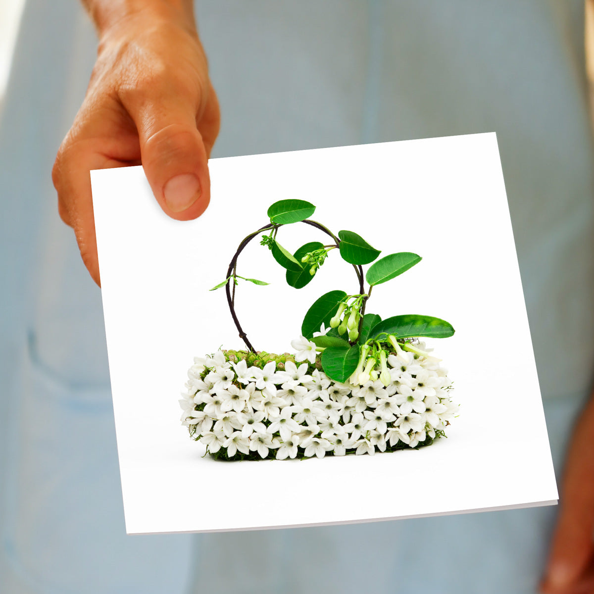 A hand held stephanotis bag greeting card by Golly Gosh Creations. Size 142 x 142 mm. Crafted from fresh stephanotis blooms on a white background.