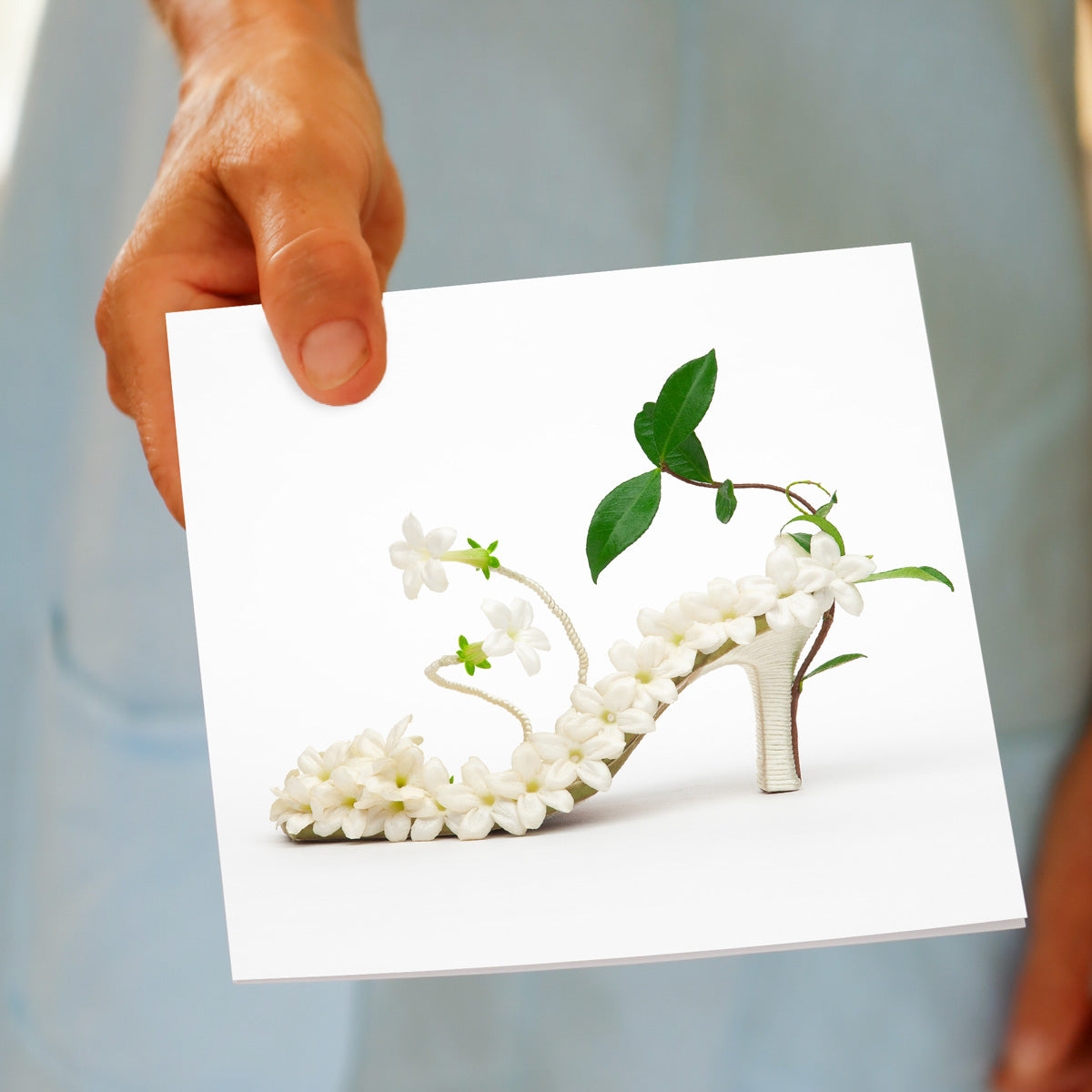 A hand held stephanotis shoe greeting card by Golly Gosh Creations. Crafted from fresh white stephanotis blossoms. Size 142 x 142 mm.