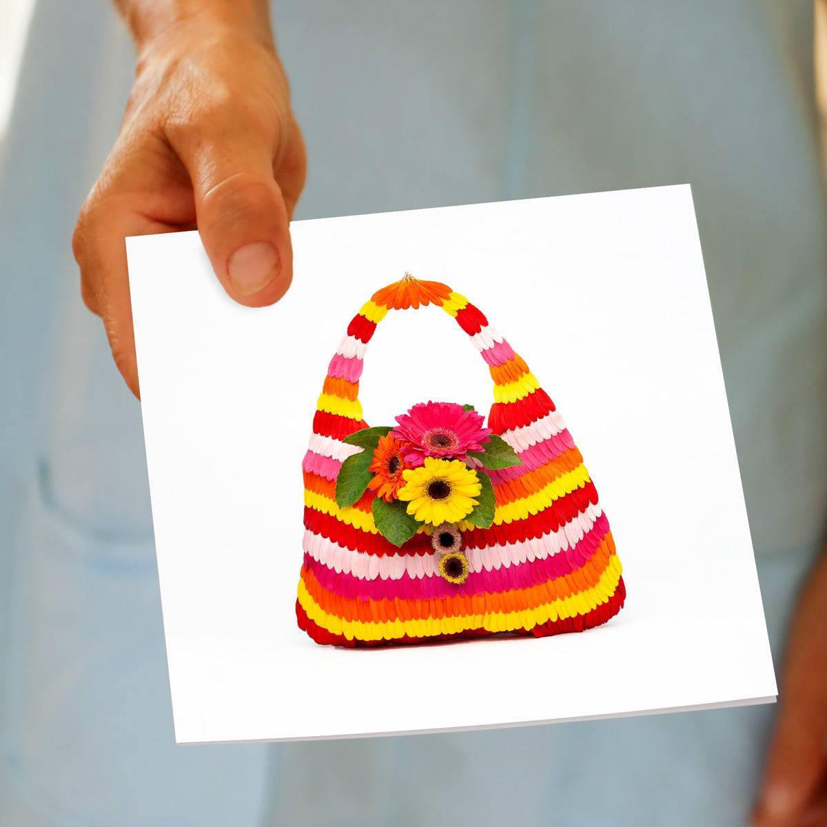 A hand held stipe gerbera petal bag greeting card from Golly Gosh Creations. A generous square card crafted from vibrant gerbera daisy petals.
