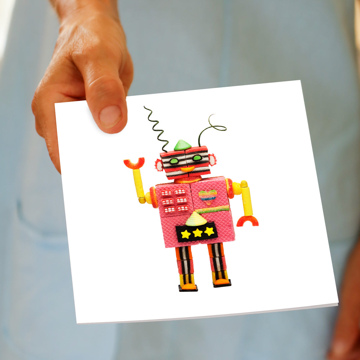 Colourful robot made from confectionery sitting on a white background. This greeting card is being held by a hand. A quality greeting card found at Golly Gosh Creations.