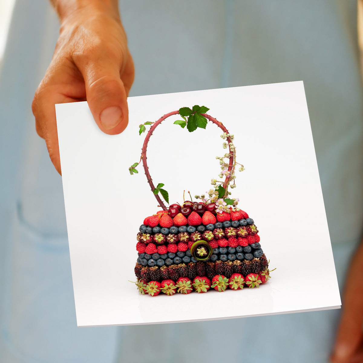 A model holds a fresh berry bag greeting card from Golly Gosh Creations. Handcrafted from fresh berries it's sitting  on a white background.