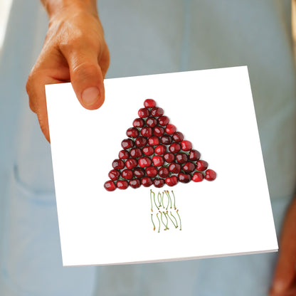 A hand holds the Christmas Cherry Tree greeting card, featuring fresh cherries built into a tree shape with a row of cherry stems below, made by Golly Gosh Creations.