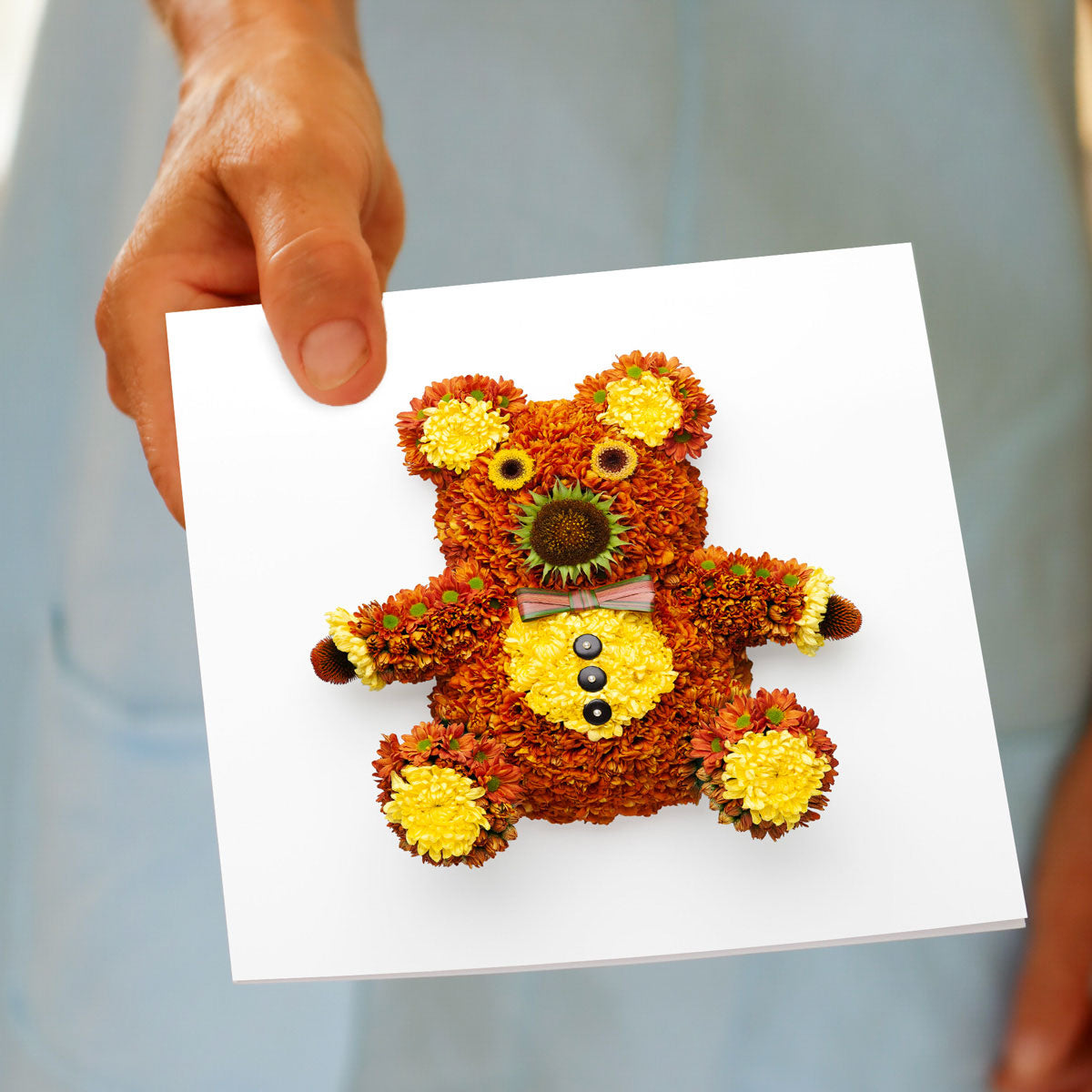 A hand held sweet chrysanthemum teddy bear greeting card from Golly Gosh Creations. Handcrafted from dainty fresh flowers. Size 142 x 142 mm