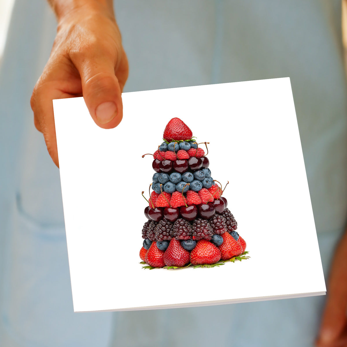 A hand holds the Christmas Mixed Berry Stack Tree greeting card, featuring strawberries, blueberries, cherries, raspberries, and blackberries layered into a tree shape, made by Golly Gosh Creations.