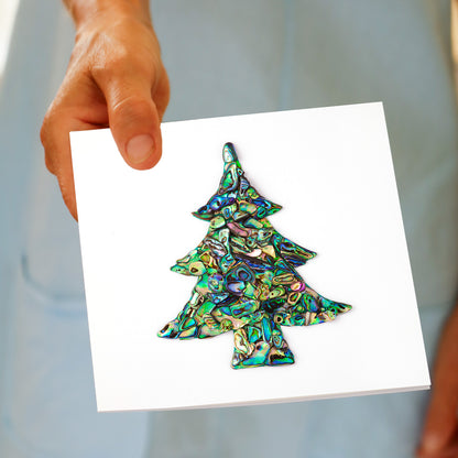 A hand holds the Christmas Paua Tree greeting card, featuring a Christmas tree shape made from iridescent paua shell pieces in green, blue, and purple, made by Golly Gosh Creations.