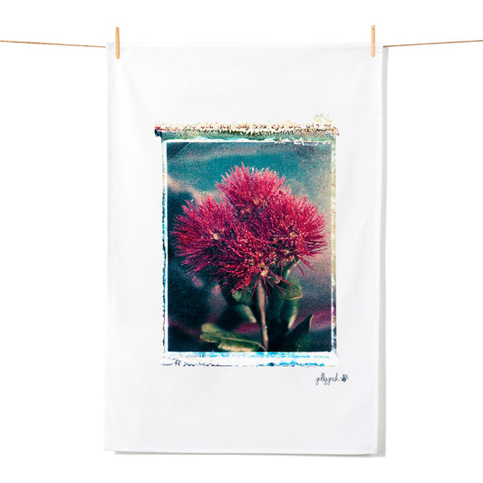 A vibrant red potutukawa flower polaroid transfer sitting on a quality cotton tea towel from Golly Gosh Creations.